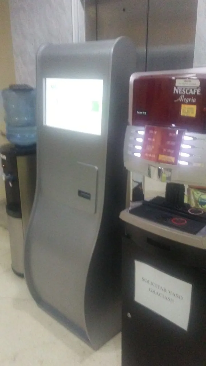 Kiosco de autoservicio real para emitir turnos junto a una máquina de café